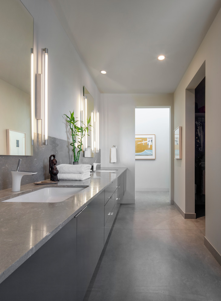 Inredning av ett modernt grå grått badrum, med släta luckor, grå skåp, vita väggar, betonggolv, ett undermonterad handfat och grått golv