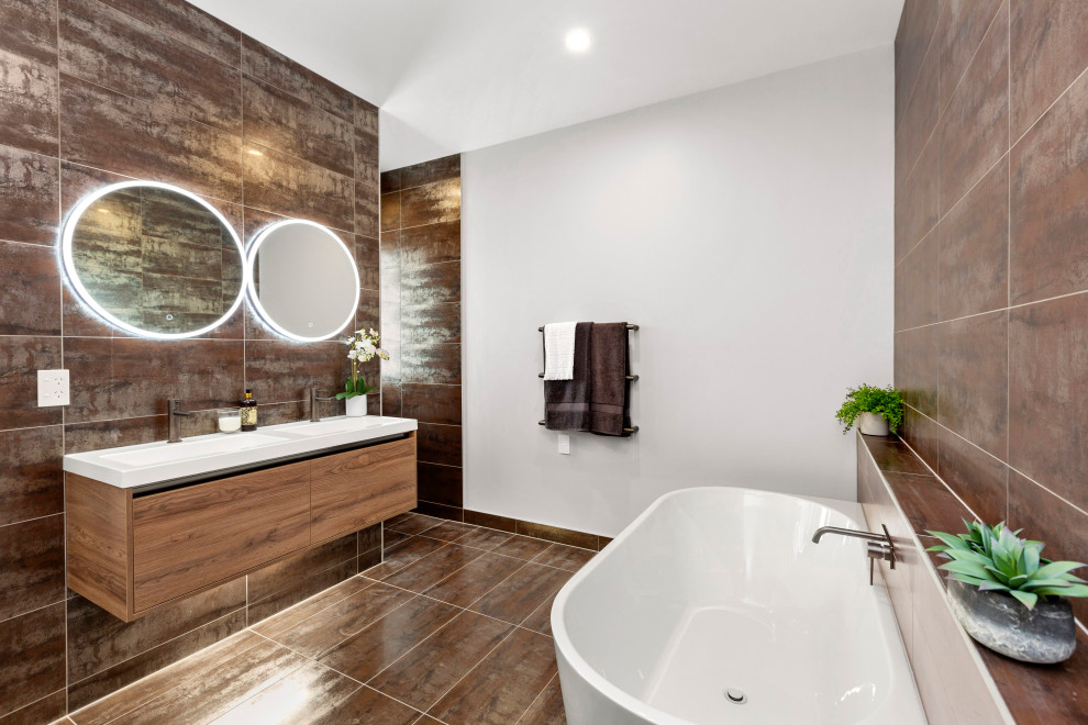 Bild på ett funkis vit vitt badrum, med släta luckor, skåp i mellenmörkt trä, ett fristående badkar, brun kakel, vita väggar, ett integrerad handfat och brunt golv