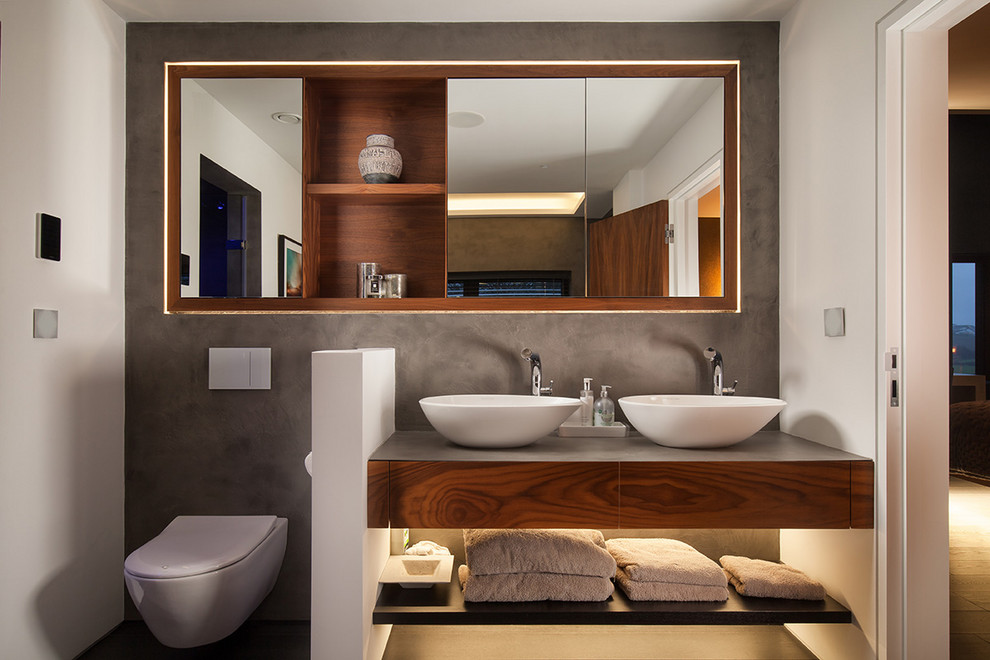 Diseño de cuarto de baño doble actual con armarios con paneles lisos, puertas de armario de madera oscura, sanitario de pared, paredes blancas y lavabo sobreencimera