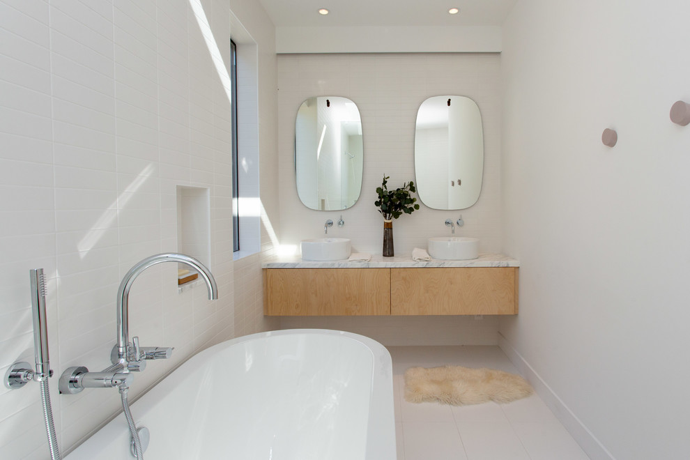 Modernes Badezimmer mit flächenbündigen Schrankfronten, hellbraunen Holzschränken, freistehender Badewanne, weißer Wandfarbe, weißem Boden und weißer Waschtischplatte in Los Angeles