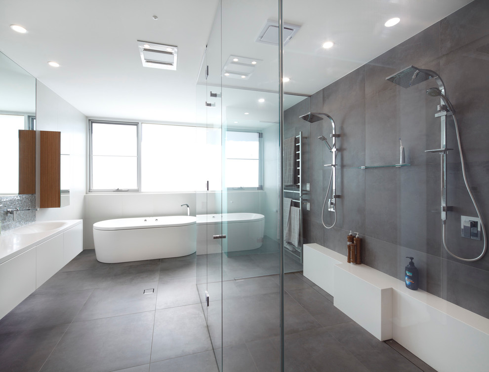 Cette image montre une salle de bain design avec un placard à porte plane, des portes de placard blanches, une baignoire indépendante, une douche double, un carrelage gris, un mur blanc, un lavabo intégré et une cabine de douche à porte battante.