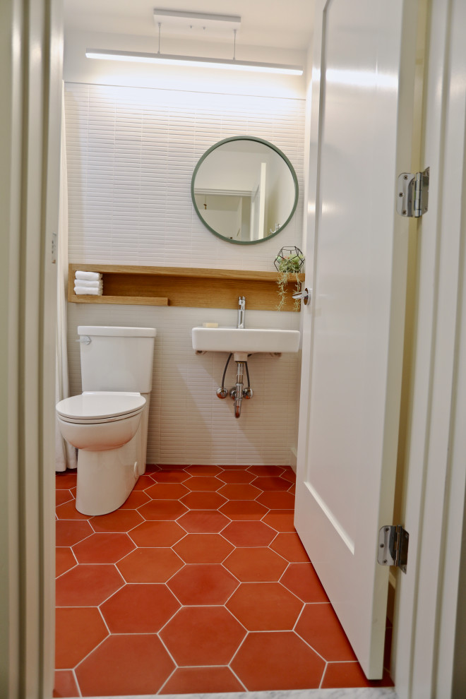 Modern inredning av ett litet badrum, med ett badkar i en alkov, en dusch/badkar-kombination, en toalettstol med separat cisternkåpa, vit kakel, porslinskakel, vita väggar, betonggolv, ett väggmonterat handfat, träbänkskiva, rött golv och dusch med duschdraperi