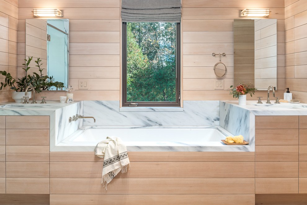 Cette photo montre une salle de bain principale montagne en bois clair avec une baignoire encastrée, un mur beige, un lavabo encastré, un plan de toilette en marbre et un carrelage blanc.