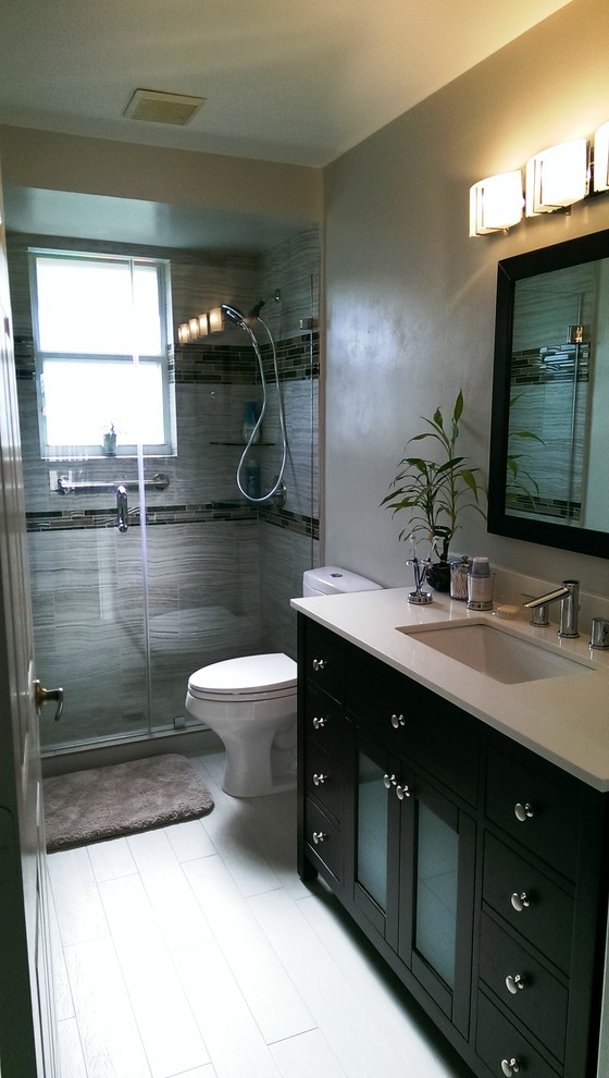 Bild på ett mellanstort funkis badrum, med ett undermonterad handfat, möbel-liknande, skåp i mellenmörkt trä, bänkskiva i kvarts, en dusch i en alkov, en toalettstol med separat cisternkåpa, brun kakel, porslinskakel, grå väggar och klinkergolv i porslin
