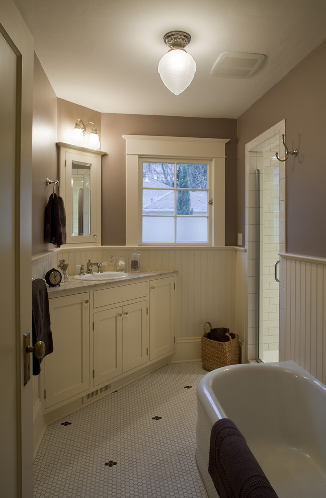 Cette image montre une petite salle de bain craftsman avec un placard à porte shaker, des portes de placard blanches, une baignoire indépendante, un carrelage noir et blanc, des carreaux de céramique, un sol en carrelage de céramique, un lavabo posé, un plan de toilette en marbre et un mur marron.