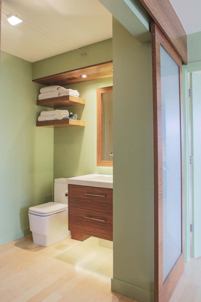 Cette photo montre une salle de bain principale tendance en bois brun de taille moyenne avec un placard à porte plane, WC à poser, un sol en carrelage de porcelaine, un lavabo intégré et un mur vert.
