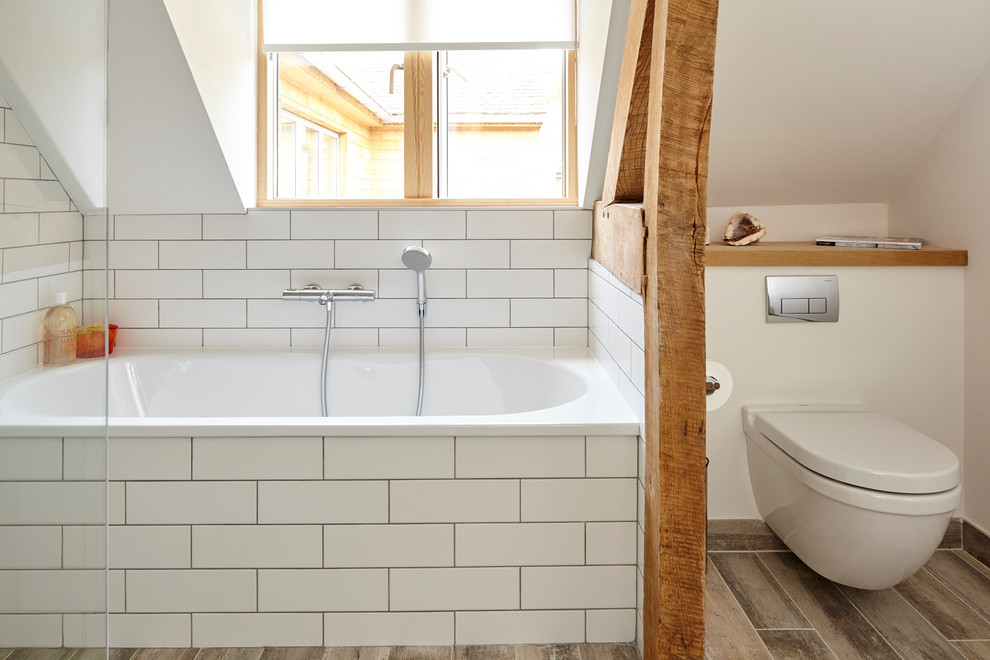 Immagine di una piccola stanza da bagno contemporanea con vasca da incasso, doccia aperta, WC sospeso, piastrelle bianche, piastrelle in ceramica, pareti bianche, pavimento con piastrelle in ceramica e top in legno