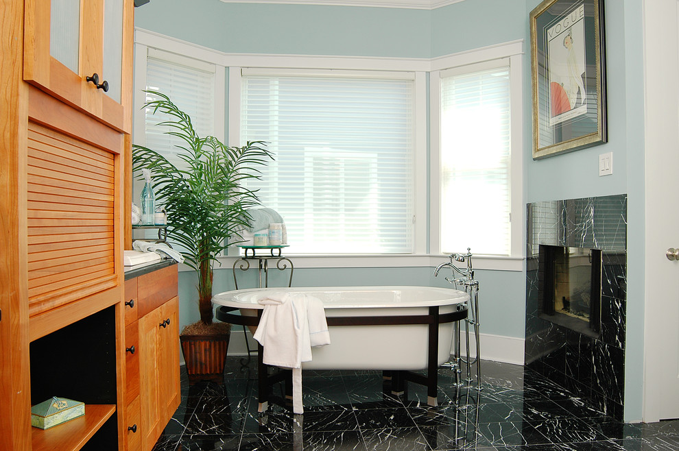 Aménagement d'une salle de bain principale bord de mer en bois brun de taille moyenne avec une baignoire indépendante, un sol noir, un placard à porte shaker et un mur bleu.