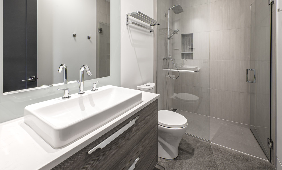 Inredning av ett modernt litet badrum med dusch, med släta luckor, grå skåp, en kantlös dusch, beige kakel, vita väggar, ett fristående handfat, grått golv, dusch med gångjärnsdörr, en toalettstol med separat cisternkåpa, porslinskakel, betonggolv och bänkskiva i akrylsten