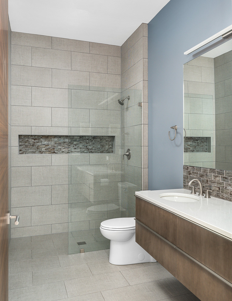 Medium sized contemporary bathroom in Chicago with flat-panel cabinets, a built-in shower, blue walls, porcelain flooring, quartz worktops, grey floors, white worktops, brown cabinets, a two-piece toilet, grey tiles, porcelain tiles, a submerged sink and an open shower.