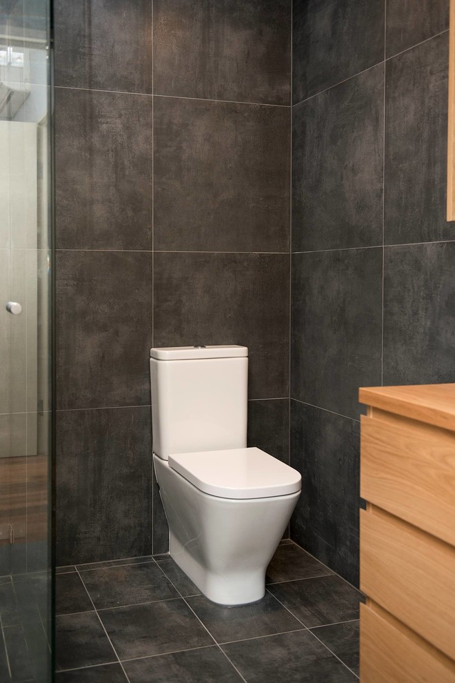 Exempel på ett mellanstort modernt en-suite badrum, med släta luckor, skåp i ljust trä, en dusch i en alkov, en toalettstol med hel cisternkåpa, grå kakel, porslinskakel, grå väggar, klinkergolv i porslin, ett fristående handfat, träbänkskiva, grått golv och dusch med gångjärnsdörr