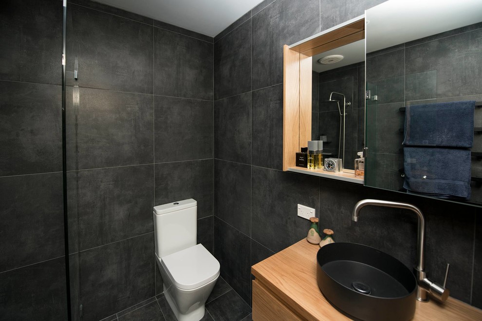 Photo of a medium sized contemporary ensuite bathroom in Sydney with flat-panel cabinets, light wood cabinets, an alcove shower, a one-piece toilet, grey tiles, porcelain tiles, grey walls, porcelain flooring, a vessel sink, wooden worktops, grey floors, a hinged door, a single sink and a floating vanity unit.