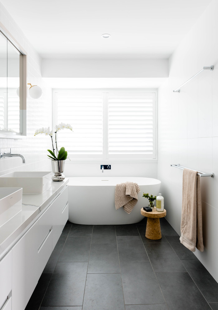 На фото: ванная комната в морском стиле с плоскими фасадами, белыми фасадами, отдельно стоящей ванной, белыми стенами, настольной раковиной, серым полом и белой столешницей