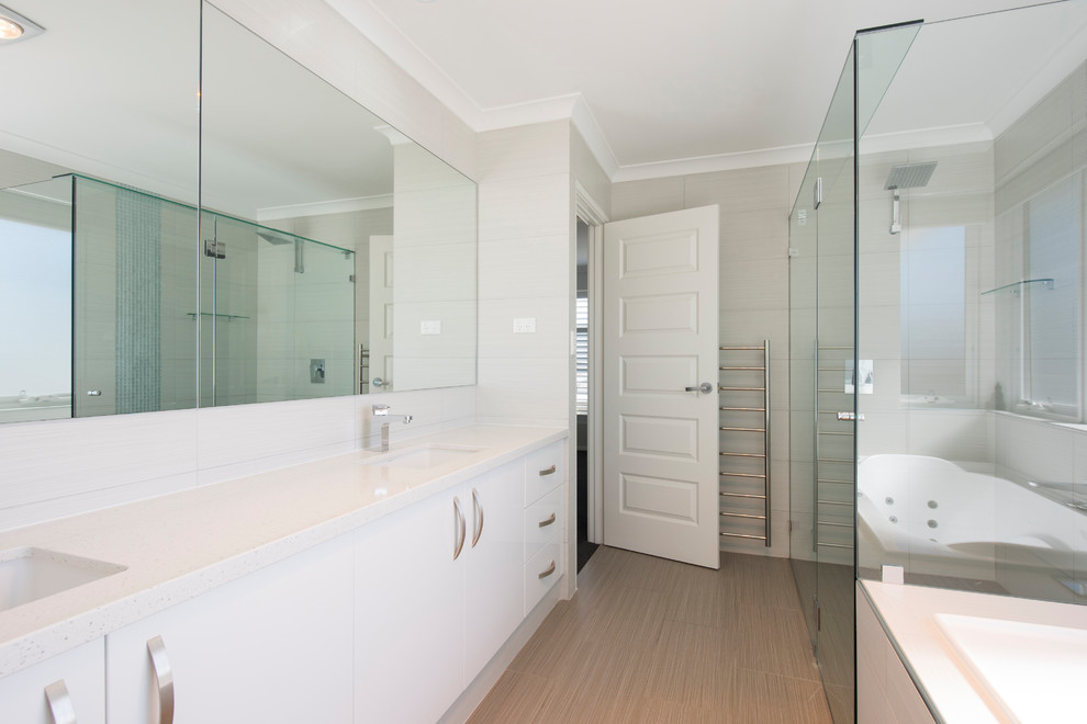 Exemple d'une grande salle de bain principale tendance avec des portes de placard blanches, une baignoire encastrée, une douche d'angle, un carrelage gris, des carreaux de céramique, un mur blanc, un sol en carrelage de céramique, un lavabo encastré et un plan de toilette en surface solide.