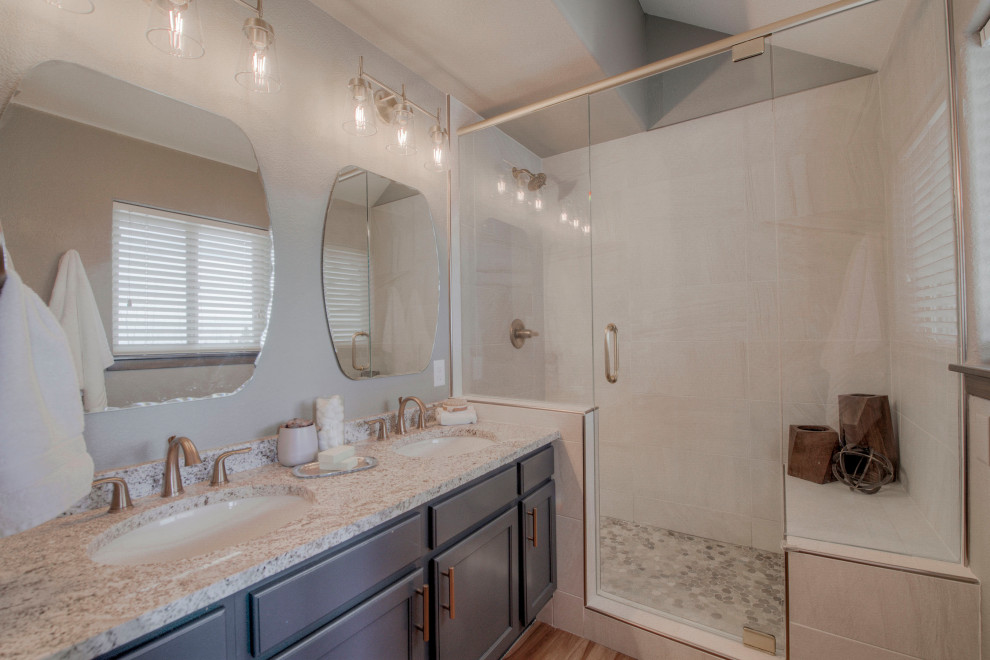 Foto på ett lantligt beige en-suite badrum, med skåp i shakerstil, blå skåp, en toalettstol med separat cisternkåpa, beige kakel, porslinskakel, grå väggar, laminatgolv, ett undermonterad handfat, granitbänkskiva, brunt golv och dusch med gångjärnsdörr
