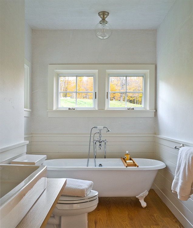 Idée de décoration pour une salle de bain design avec une baignoire sur pieds, un mur blanc et un sol en bois brun.