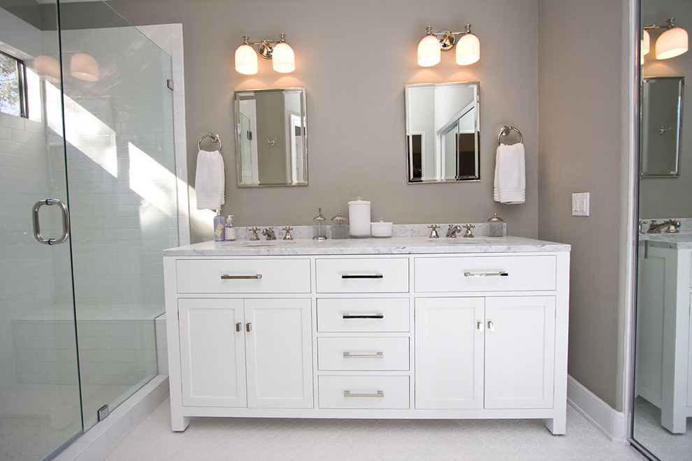 Cette image montre une salle de bain design avec un lavabo encastré, un placard à porte shaker, des portes de placard blanches, un plan de toilette en marbre, une douche d'angle, un carrelage blanc, un carrelage métro et un mur gris.