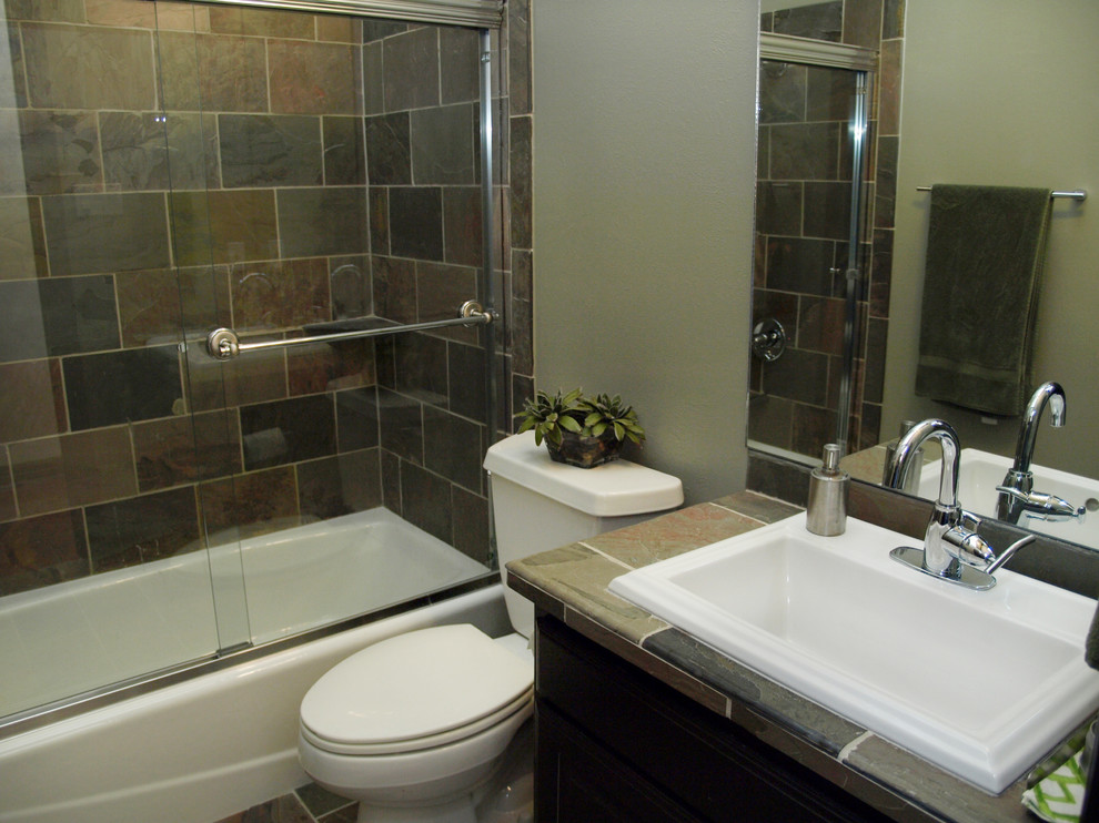 Modern inredning av ett litet badrum, med släta luckor, ett badkar i en alkov, en dusch/badkar-kombination, en toalettstol med separat cisternkåpa, beige kakel, grå kakel, skifferkakel, skiffergolv, ett nedsänkt handfat, kaklad bänkskiva, bruna skåp och grå väggar