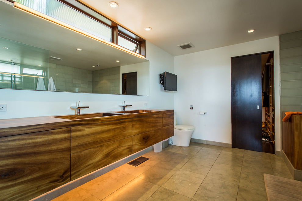 Example of a large trendy master green tile and porcelain tile travertine floor bathroom design in Los Angeles with flat-panel cabinets, medium tone wood cabinets, a one-piece toilet, white walls, wood countertops and a drop-in sink