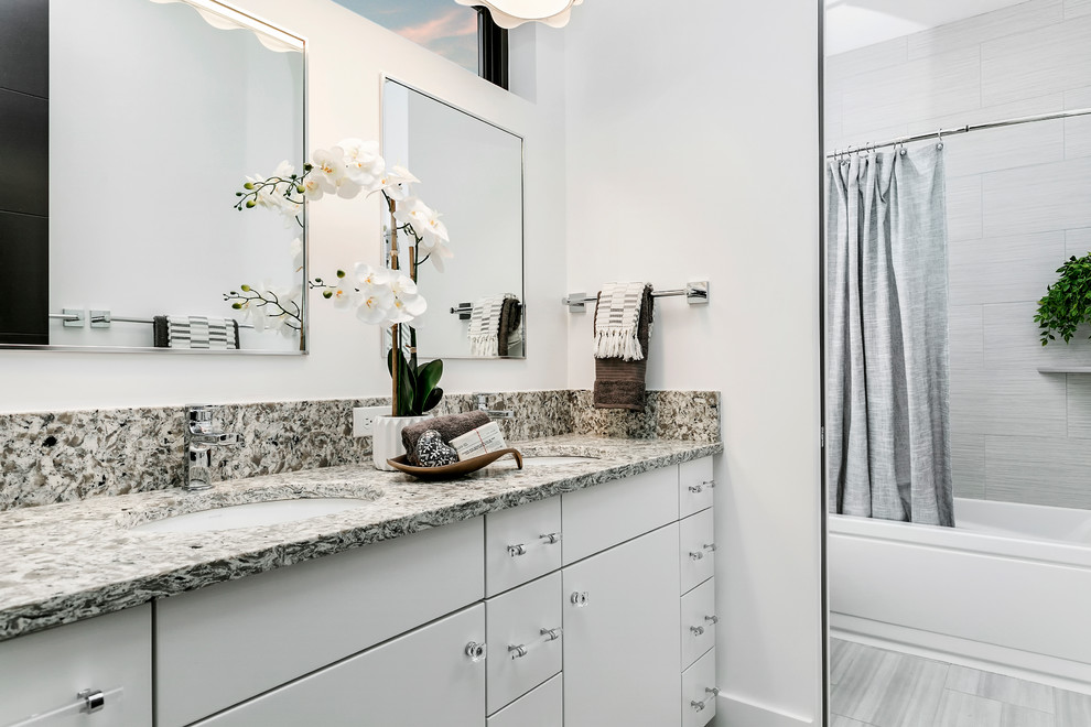 Example of a mid-sized trendy gray tile and porcelain tile porcelain tile and gray floor bathroom design in Boise with flat-panel cabinets, white cabinets, a two-piece toilet, white walls, an undermount sink, granite countertops and multicolored countertops