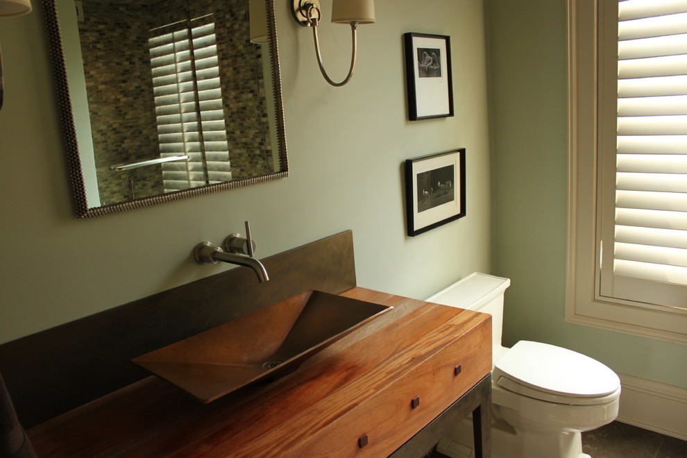 Aménagement d'une salle d'eau contemporaine en bois brun de taille moyenne avec un placard à porte affleurante, WC à poser, un mur vert, un sol en carrelage de porcelaine, une vasque, un plan de toilette en bois et un sol noir.
