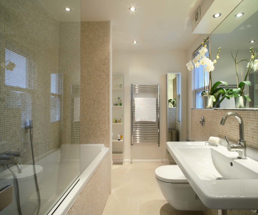 Design ideas for a medium sized contemporary half tiled bathroom in London with a wall-mounted sink, a built-in bath, a shower/bath combination, a one-piece toilet, beige tiles, mosaic tiles, beige walls and beige floors.