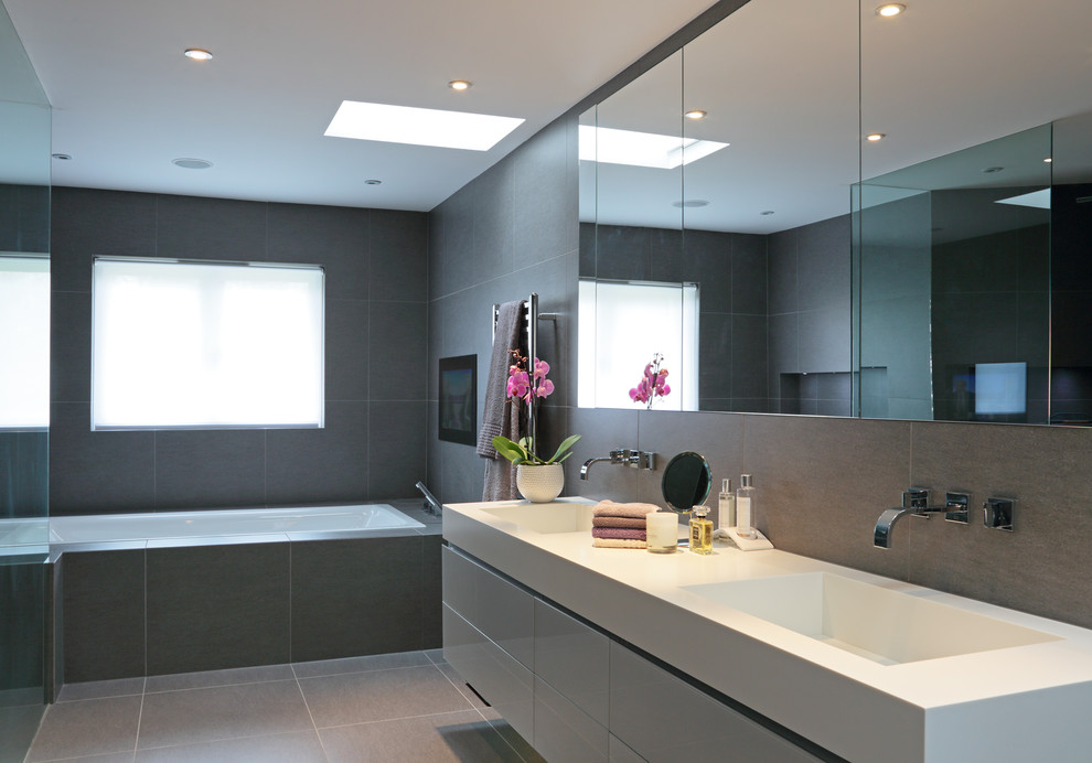 Bild på ett funkis badrum, med ett integrerad handfat, ett badkar i en alkov och grå kakel