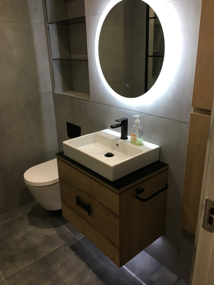 Bild på ett mellanstort funkis svart svart badrum med dusch, med luckor med upphöjd panel, skåp i mellenmörkt trä, en öppen dusch, en vägghängd toalettstol, grå kakel, porslinskakel, grå väggar, klinkergolv i porslin, ett nedsänkt handfat, bänkskiva i glas, grått golv och med dusch som är öppen