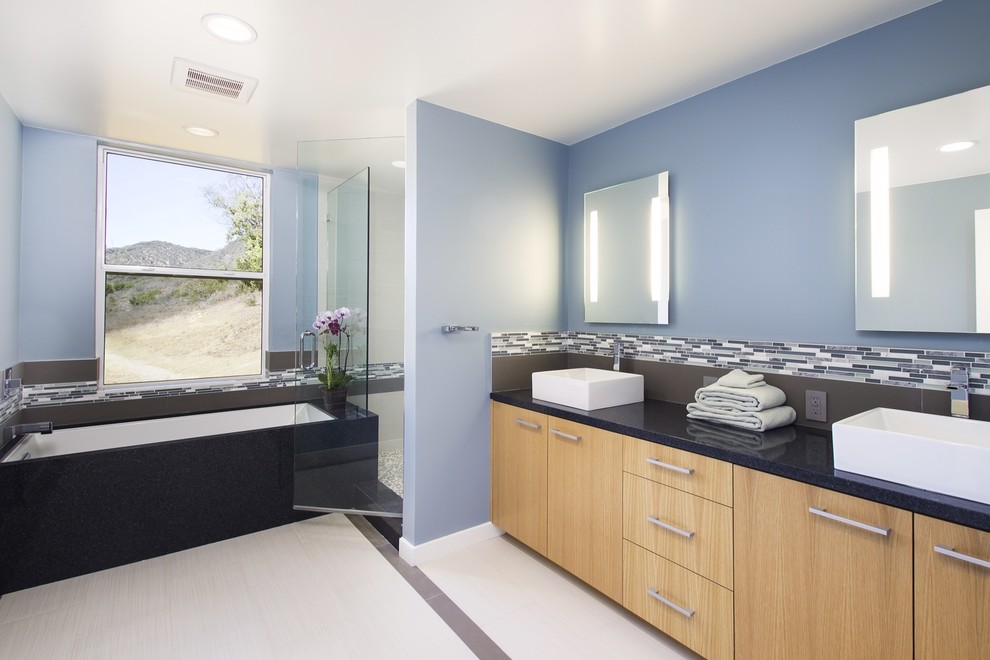 Example of a mid-sized trendy master black tile and glass tile ceramic tile and white floor alcove shower design in Los Angeles with a vessel sink, flat-panel cabinets, light wood cabinets, granite countertops, an undermount tub, a one-piece toilet, blue walls and a hinged shower door