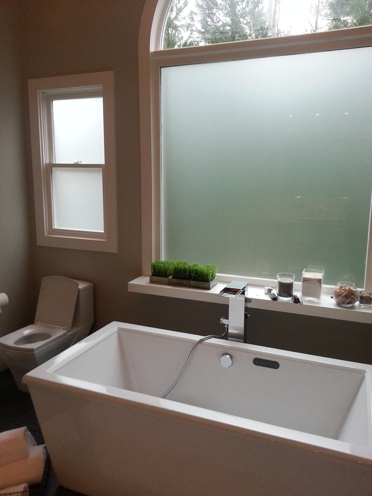 Inredning av ett modernt en-suite badrum, med ett avlångt handfat, släta luckor, vita skåp, bänkskiva i betong, ett fristående badkar, en öppen dusch, en toalettstol med hel cisternkåpa, grå kakel, glaskakel, grå väggar och klinkergolv i porslin