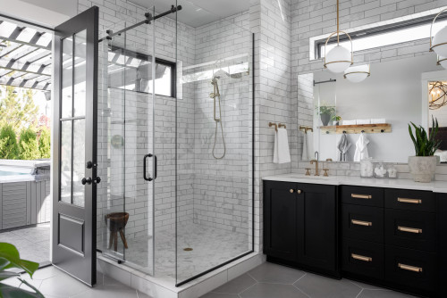Modern bathroom with Black Bathroom Cabinets, white subway tile shower, glass enclosure, and gold fixtures