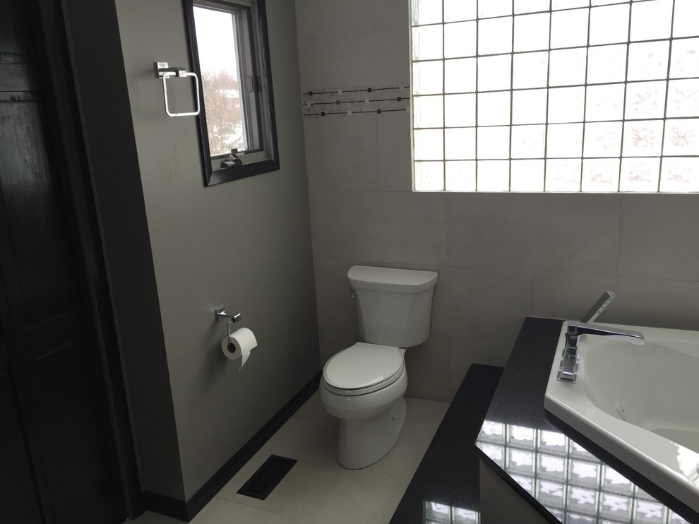 Foto på ett mellanstort funkis en-suite badrum, med svarta skåp, ett hörnbadkar, en toalettstol med separat cisternkåpa, svart och vit kakel, porslinskakel, grå väggar, klinkergolv i porslin, ett undermonterad handfat, granitbänkskiva och en dusch i en alkov