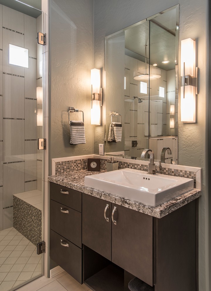 Cette image montre une grande salle de bain principale design en bois foncé avec une vasque, un placard à porte plane, un plan de toilette en granite, une douche double, un carrelage gris, des carreaux de céramique, un mur gris et un sol en carrelage de céramique.