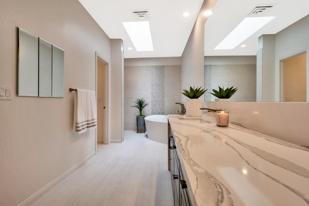 Photo of a large contemporary ensuite bathroom in Phoenix with raised-panel cabinets, black cabinets, a freestanding bath, a walk-in shower, grey tiles, porcelain tiles, grey walls, porcelain flooring, a submerged sink, engineered stone worktops, grey floors, an open shower and white worktops.