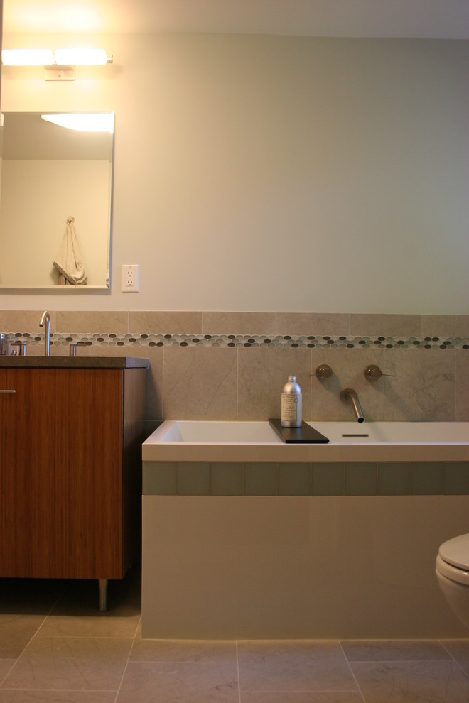 Photo of a small modern ensuite bathroom in New York with flat-panel cabinets, medium wood cabinets, a freestanding bath, grey tiles, stone tiles, a submerged sink, limestone worktops, grey walls and limestone flooring.