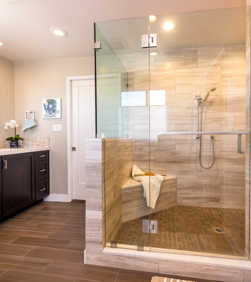 This is an example of a large contemporary ensuite bathroom in Los Angeles with a built-in shower, recessed-panel cabinets, dark wood cabinets, beige tiles, travertine tiles, beige walls, vinyl flooring, a submerged sink, engineered stone worktops, brown floors and a hinged door.