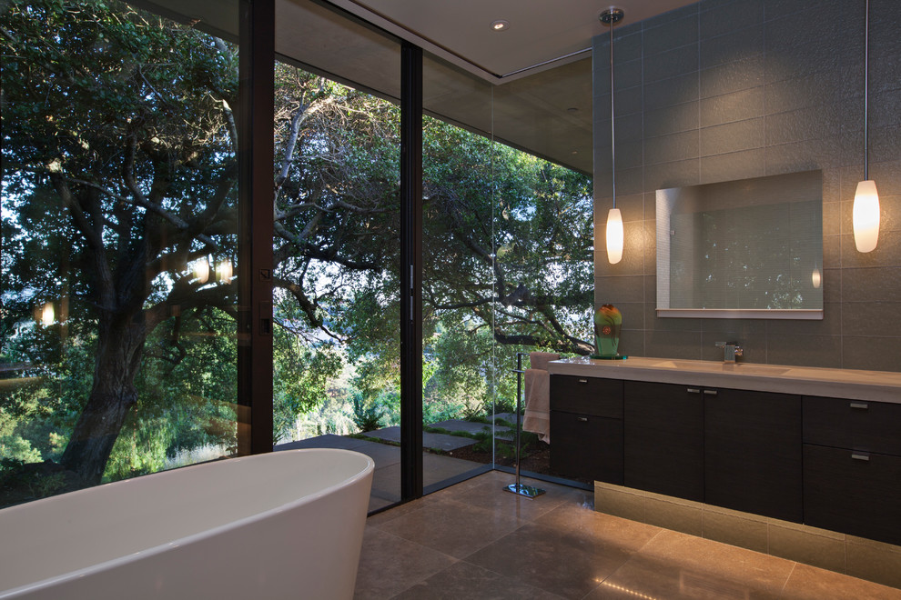 Пример оригинального дизайна: огромная ванная комната в стиле модернизм с плоскими фасадами, темными деревянными фасадами, отдельно стоящей ванной, душем в нише, инсталляцией, черно-белой плиткой, стеклянной плиткой, полом из травертина, монолитной раковиной и столешницей из бетона
