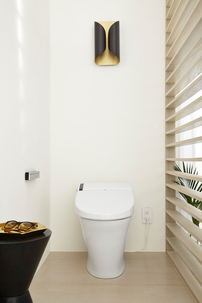 Cette photo montre un WC et toilettes tendance en bois clair de taille moyenne avec un placard à porte plane, un bidet, un mur blanc, parquet clair, un lavabo intégré et un plan de toilette en béton.