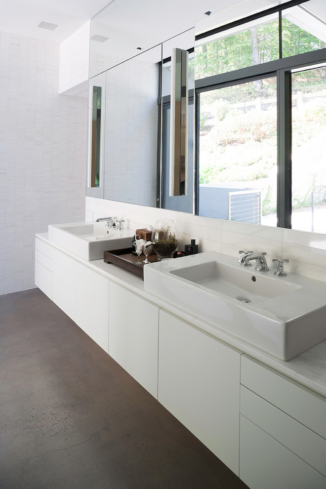 Inredning av ett modernt badrum, med ett fristående handfat, släta luckor, vita skåp, vita väggar och betonggolv