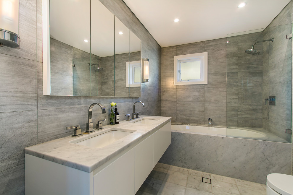 Large trendy master gray tile and stone slab marble floor and gray floor bathroom photo in Chicago with flat-panel cabinets, white cabinets, an undermount tub, a two-piece toilet, gray walls, an undermount sink and marble countertops