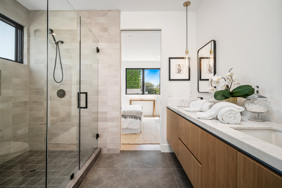 Contemporary bathroom in Los Angeles with flat-panel cabinets, medium wood cabinets, an alcove shower, white walls, a submerged sink, grey floors, a hinged door, white worktops and double sinks.