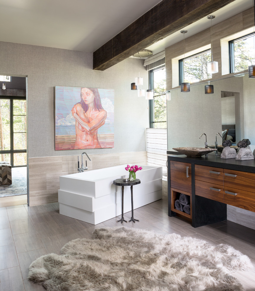 Idée de décoration pour une salle de bain principale design en bois brun avec une baignoire indépendante, un carrelage beige, une vasque, un plan de toilette noir, meuble double vasque, poutres apparentes et du papier peint.
