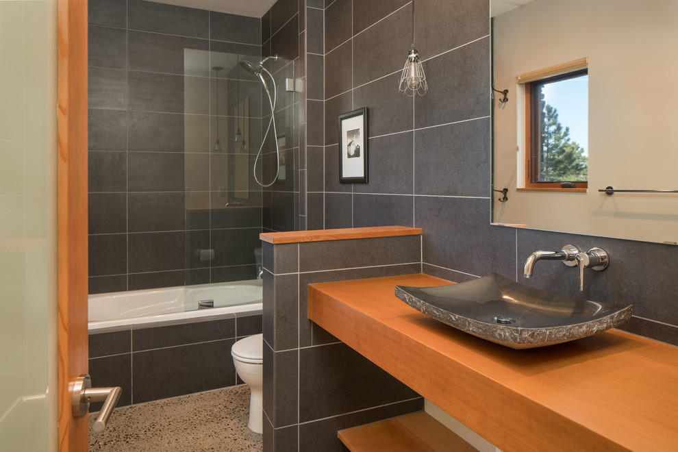 Modern inredning av ett mellanstort brun brunt badrum, med öppna hyllor, skåp i ljust trä, en dusch/badkar-kombination, grå kakel, porslinskakel, beige väggar, ett fristående handfat, träbänkskiva och med dusch som är öppen