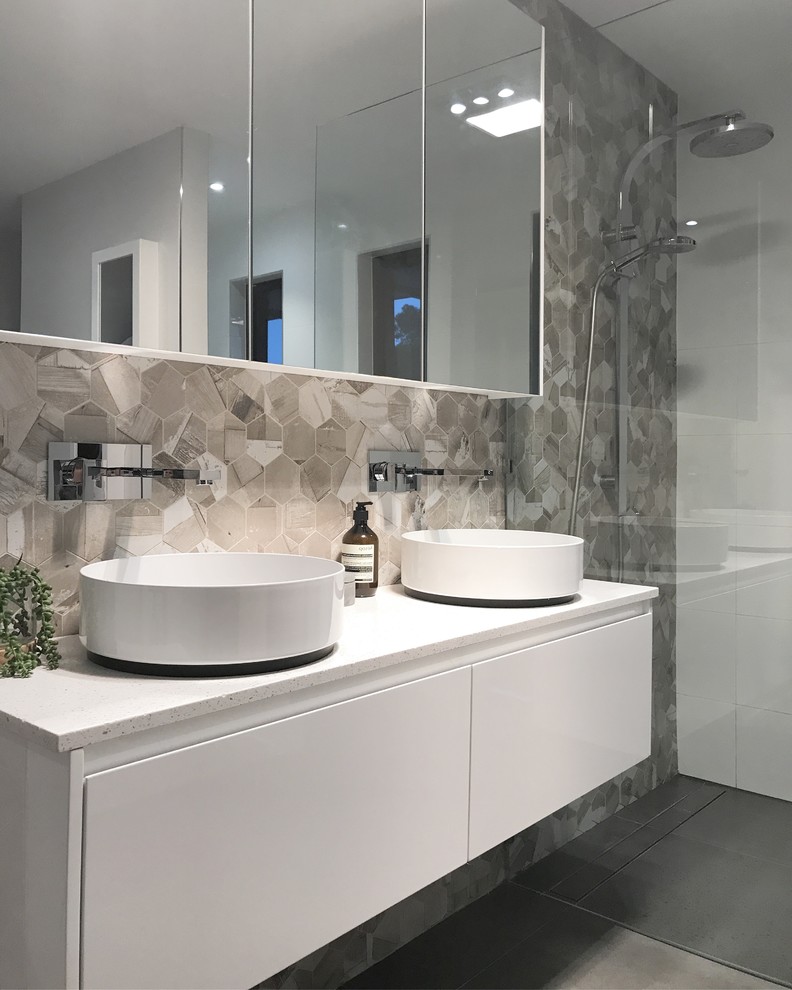 Exemple d'une salle de bain tendance avec un placard à porte plane, des portes de placard blanches, un carrelage gris, un mur blanc, une vasque, un sol gris et un plan de toilette blanc.