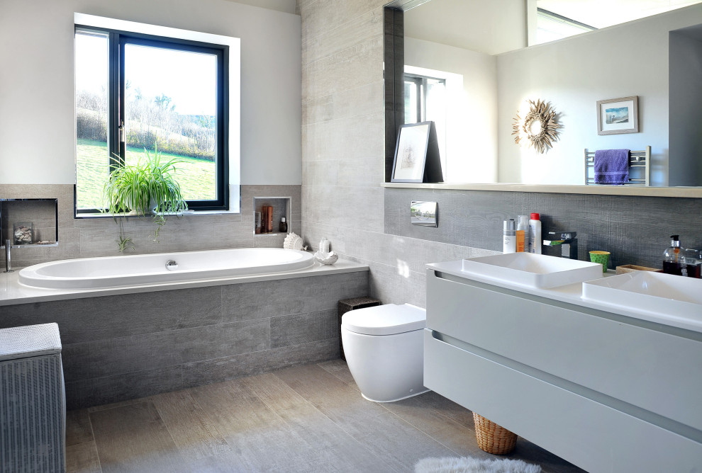 Exemple d'une salle de bain moderne de taille moyenne pour enfant avec un placard à porte plane, des portes de placard grises, une baignoire posée, WC à poser, un carrelage gris, un carrelage imitation parquet, un mur gris, un sol en carrelage imitation parquet, un lavabo posé, un sol gris, un plan de toilette blanc, meuble double vasque et meuble-lavabo suspendu.