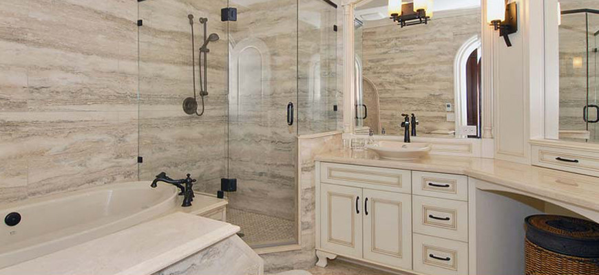 Inredning av ett modernt stort badrum, med ett fristående handfat, luckor med profilerade fronter, vita skåp, granitbänkskiva, ett platsbyggt badkar, en hörndusch, beige kakel, stenhäll och beige väggar