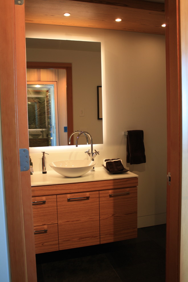Cette image montre une grande salle d'eau design en bois brun avec un placard à porte plane, un plan de toilette en quartz modifié, un carrelage blanc, un mur gris, une vasque, un sol noir et un plan de toilette blanc.