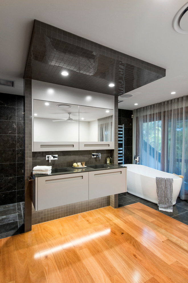 Esempio di una grande stanza da bagno padronale minimal con vasca freestanding, piastrelle grigie e pavimento in legno massello medio