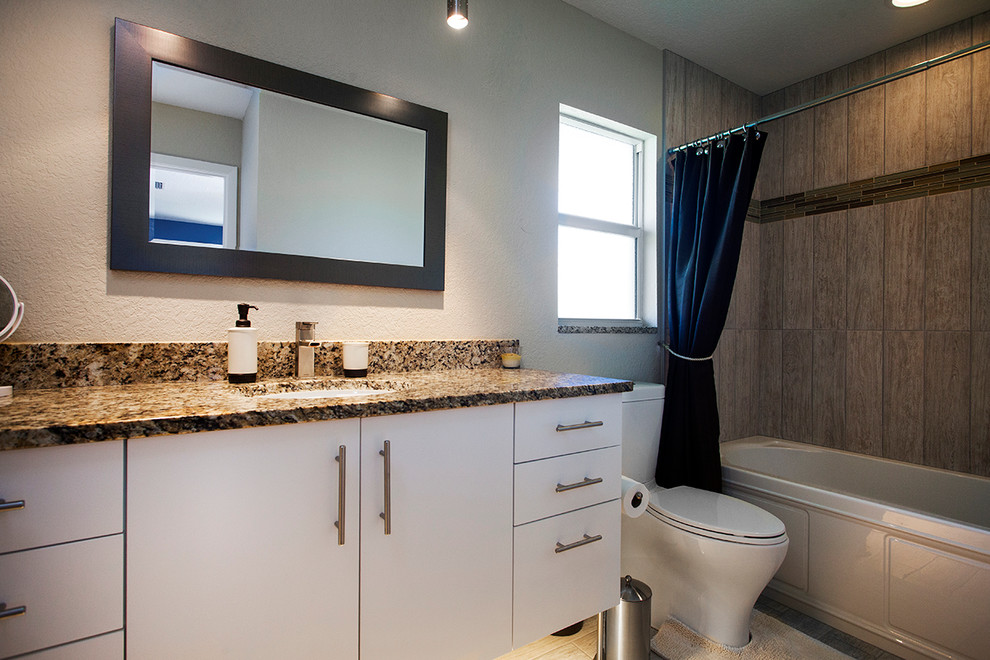На фото: ванная комната в современном стиле с плоскими фасадами, белыми фасадами, столешницей из гранита, ванной в нише, унитазом-моноблоком, керамической плиткой и полом из керамической плитки с