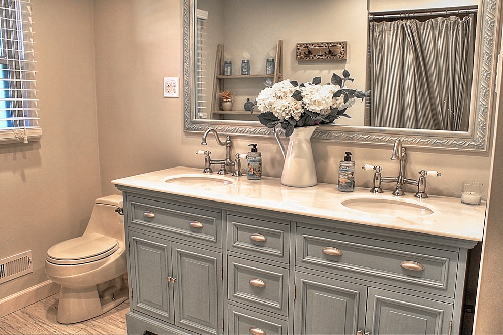 Lantlig inredning av ett stort vit vitt en-suite badrum, med ett undermonterad handfat, möbel-liknande, blå skåp, marmorbänkskiva, en dusch/badkar-kombination, en toalettstol med hel cisternkåpa, keramikplattor, beige väggar, klinkergolv i keramik, ett badkar i en alkov, grå kakel, beiget golv och dusch med duschdraperi